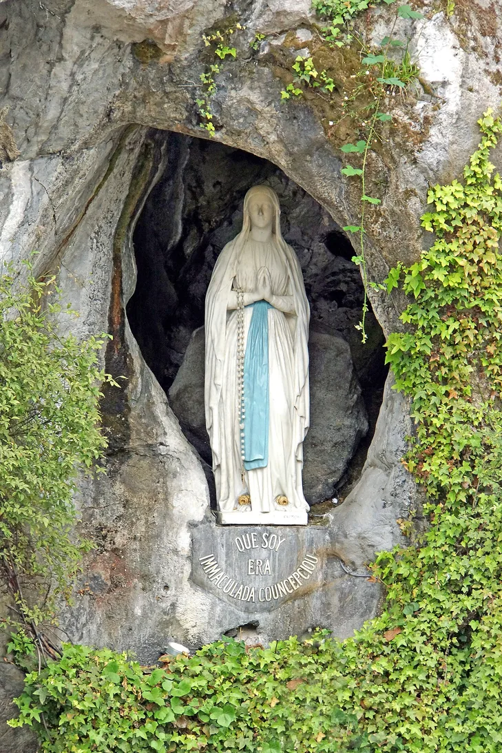 Statue de Notre-Dame de Lourdes dans une niche rocheuse.